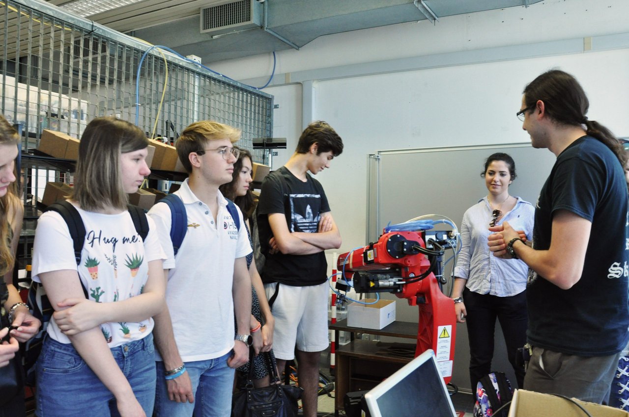 Foto dell'edizione 2025 di techcamp: un professore spiega ad un gruppo di ragazzi il funzionamento di una macchinario