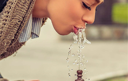 [Translate to English:] ragazza che beve acqua da una fontana